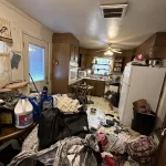 Interior view of a heavily cluttered and messy kitchen with items piled on all surfaces.